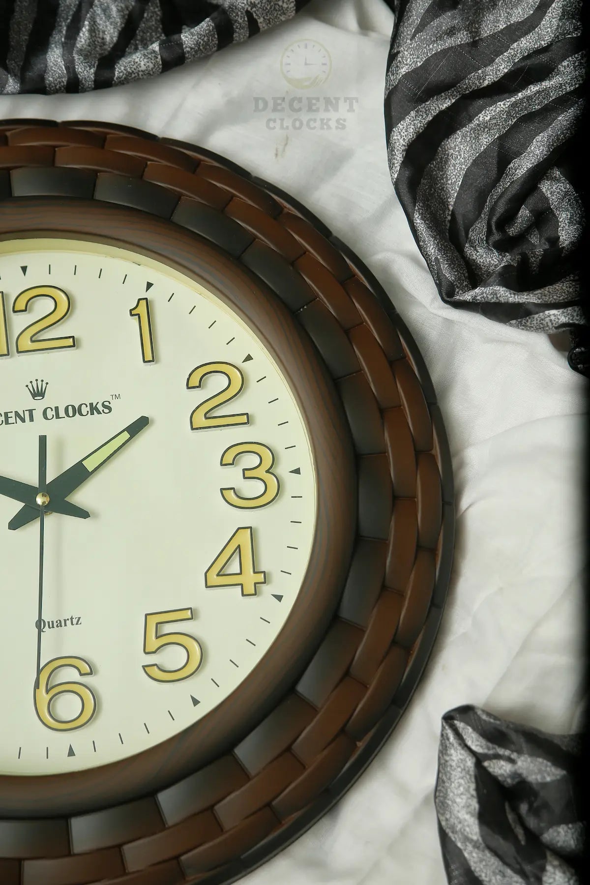 Wall clock with brown frame and white face on a marble surface with decorative fabric.